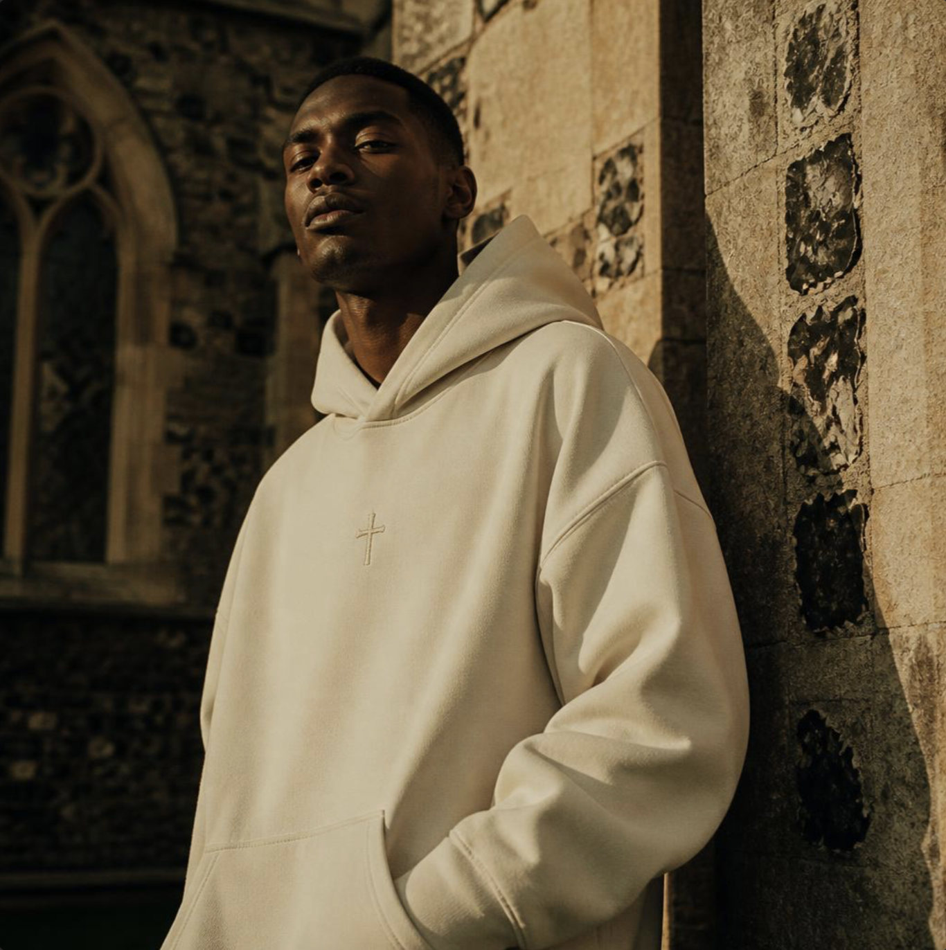 Model in a cream Holy Water hoodie against a cathedral wall